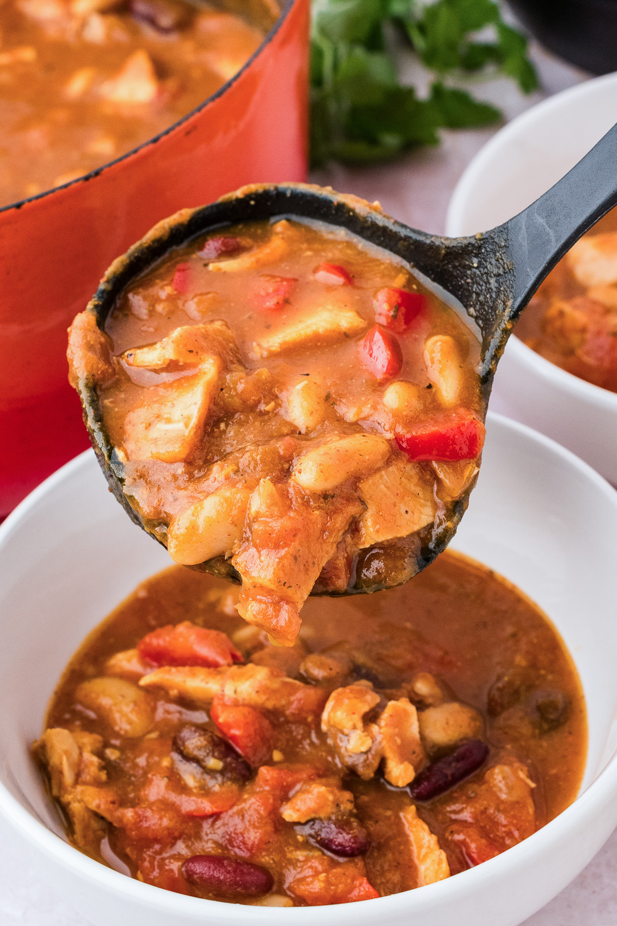 A ladle filled with leftover turkey pumpkin chili being poured into a white bowl.