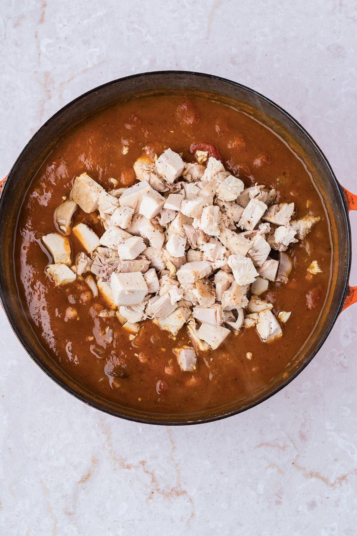 Diced cooked turkey in a pot of pumpkin chili.