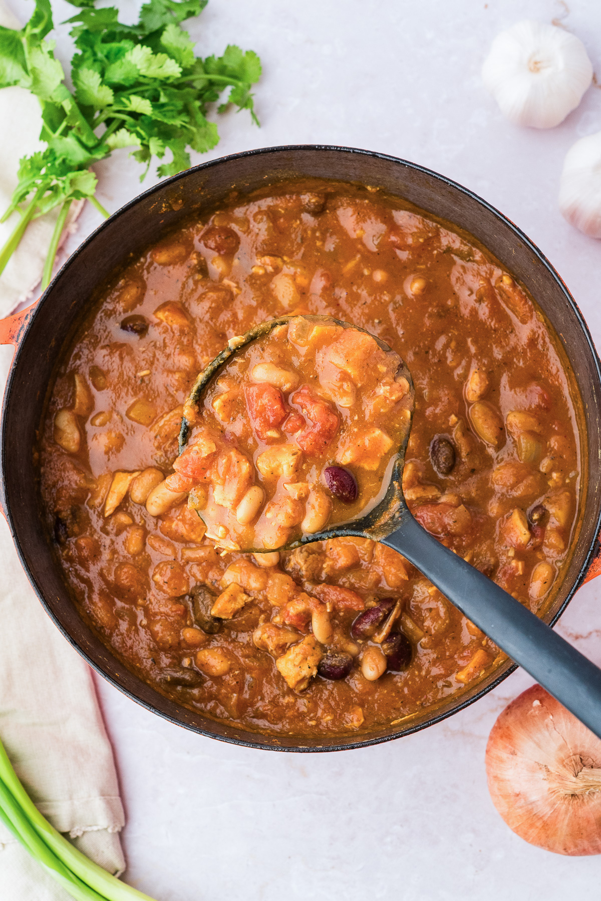 A ladle scoops leftover turkey pumpkin chili from a large pot.