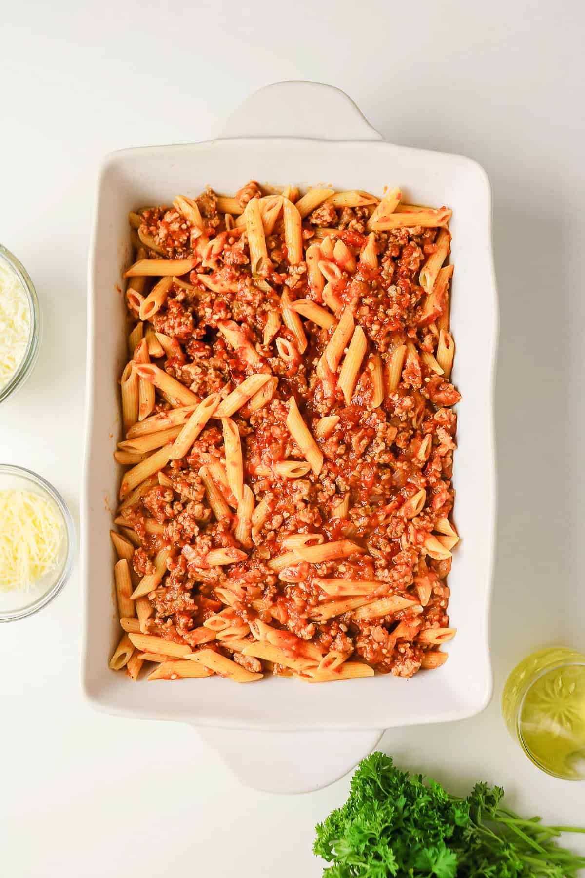 Penne sausage pasta bake with meat sauce in a white rectangular baking dish.