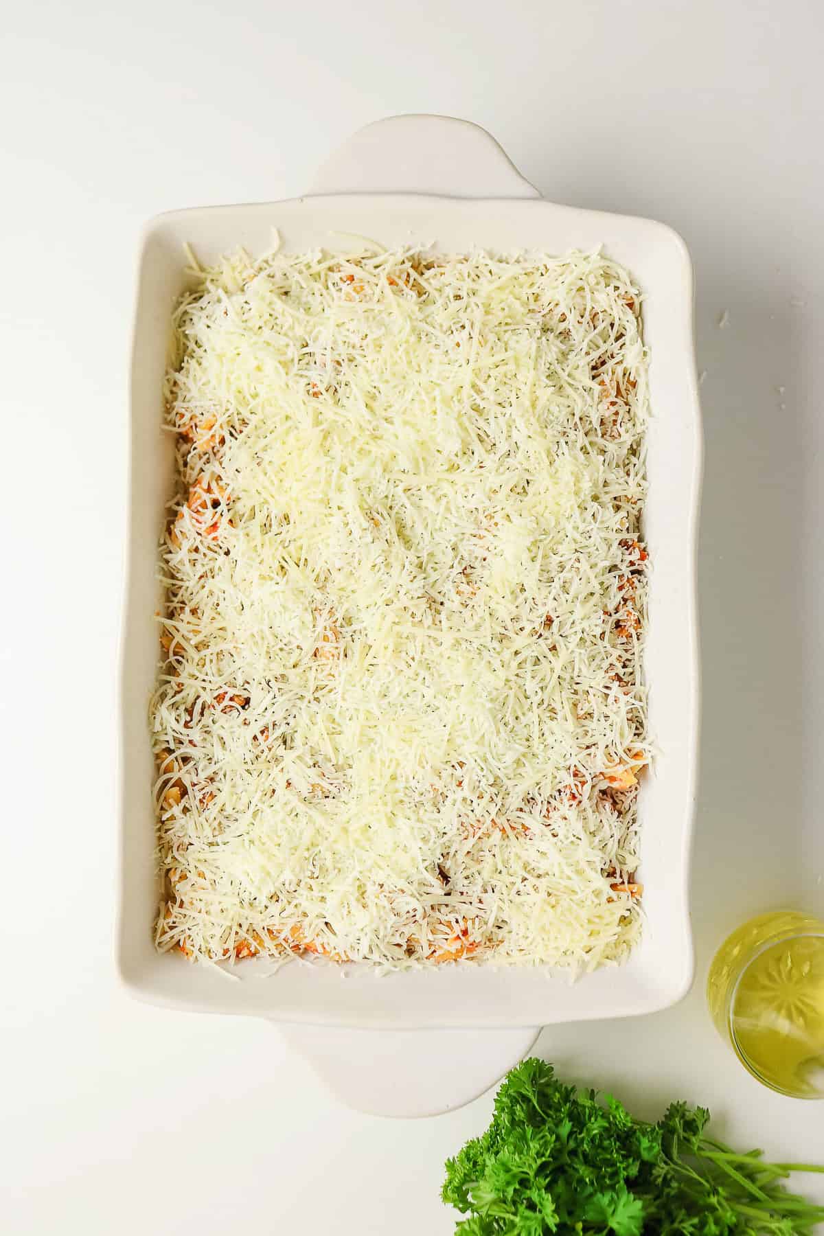 A rectangular baking dish filled with a sausage pasta bake topped with shredded cheese.