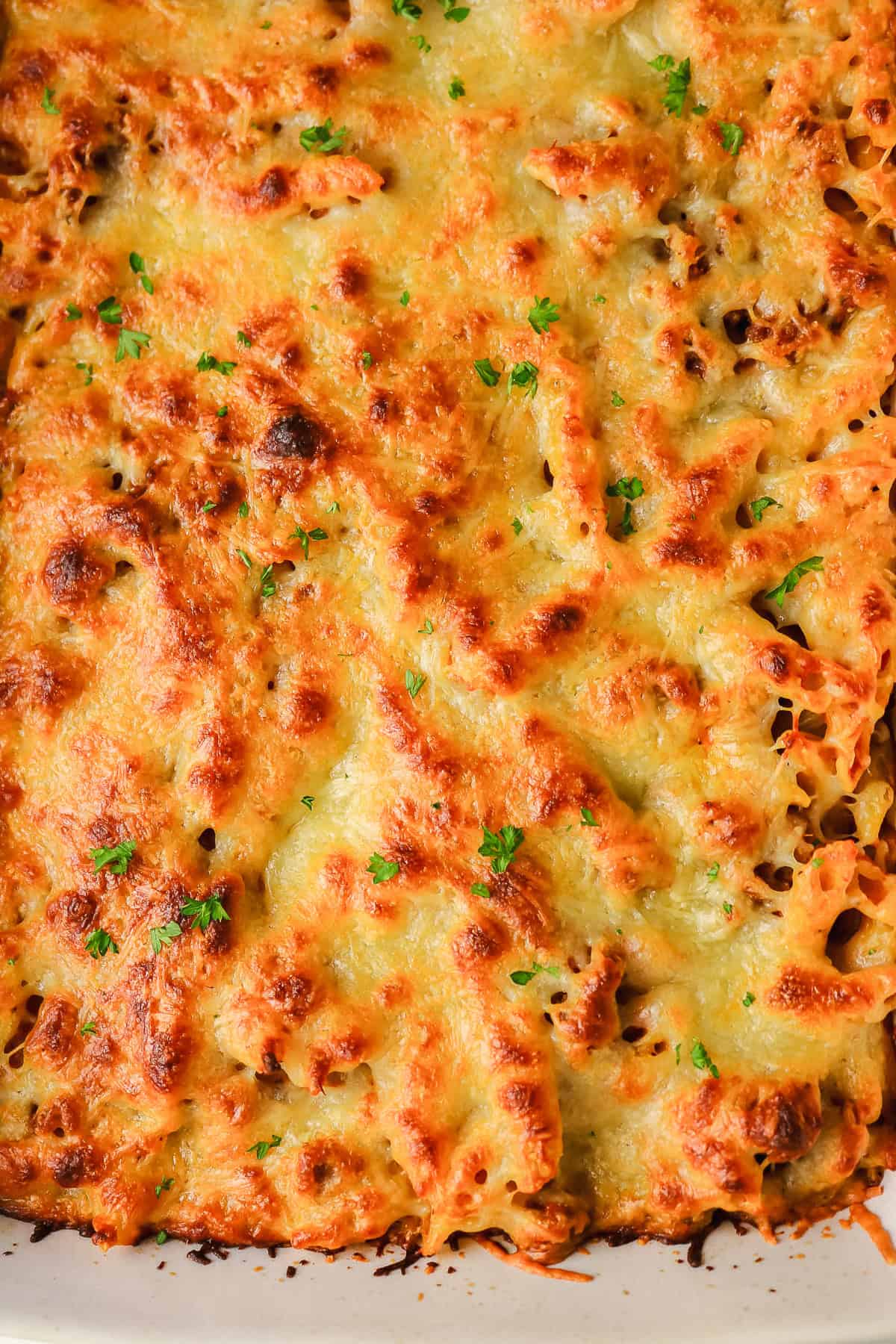 Baked sausage pasta topped with melted, golden-brown cheese and garnished with parsley.
