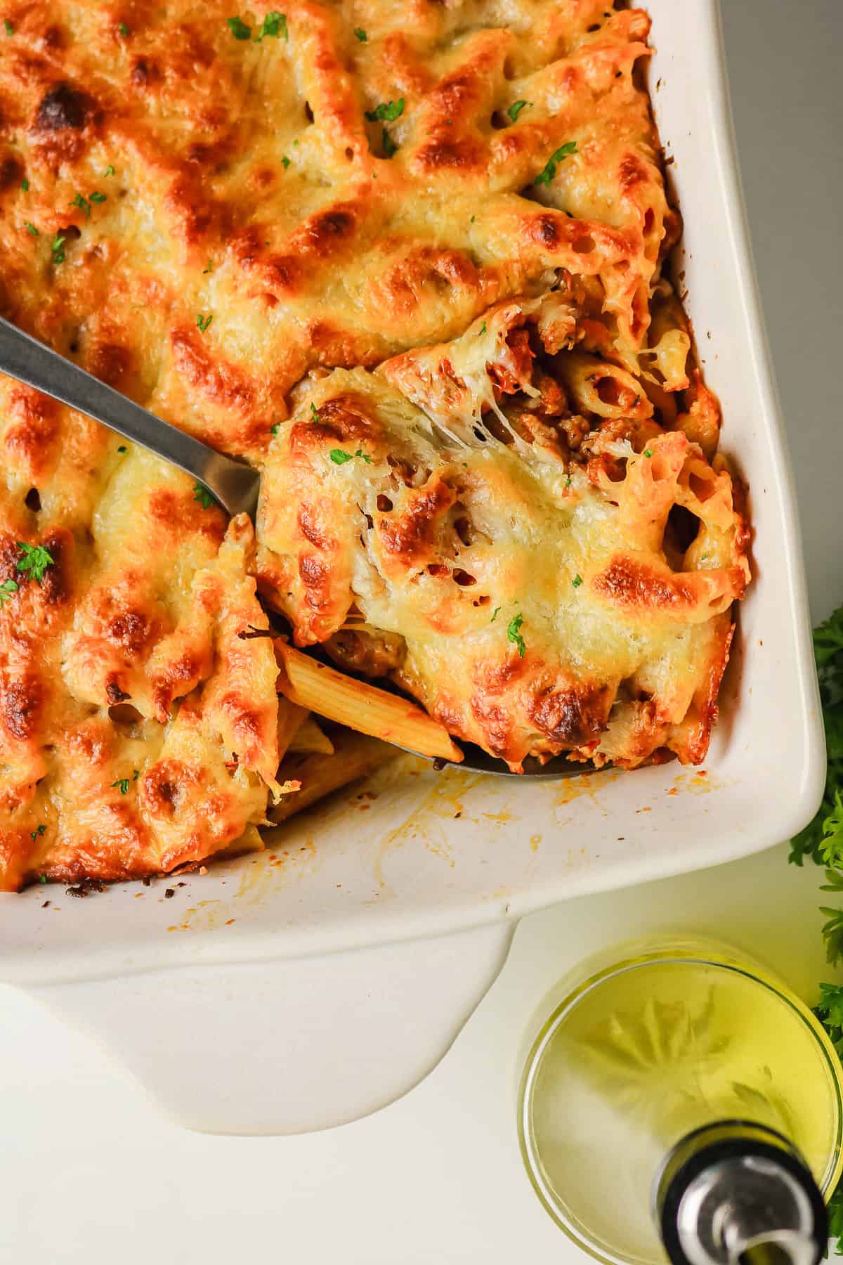 A spoon scoops into a sausage pasta bake in a casserole dish topped with a melted cheese crust.