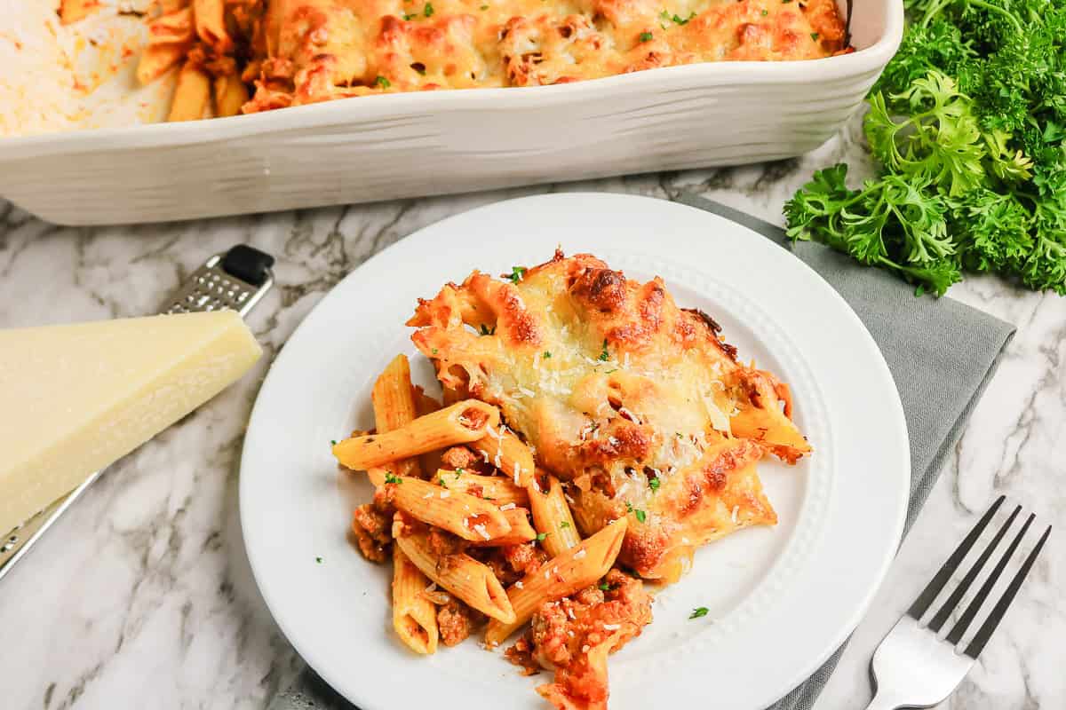 A serving of sausage pasta bake with meat sauce and melted cheese on a white plate.