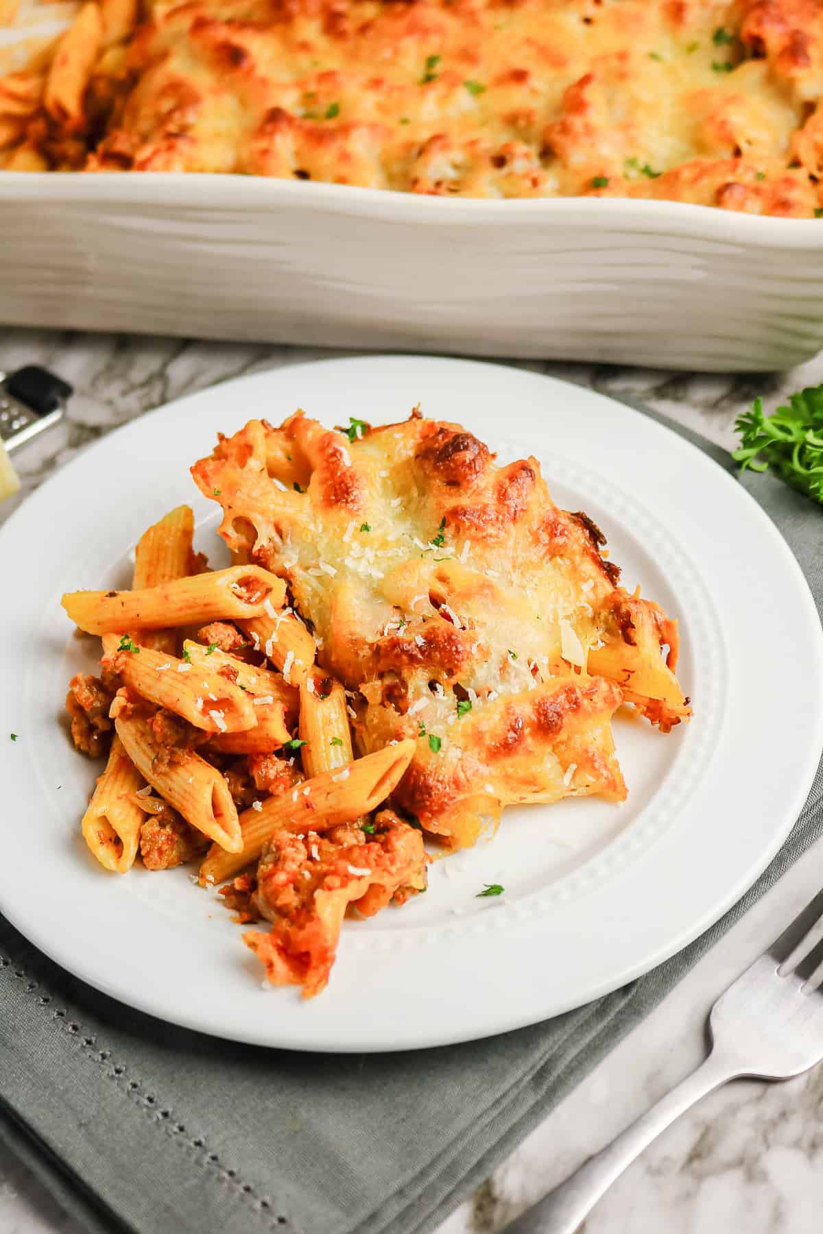 A serving of sausage pasta bake with meat sauce and melted cheese on a white plate.