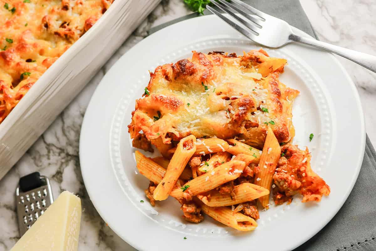 A serving of baked sausage pasta with meat sauce and melted cheese on a plate.