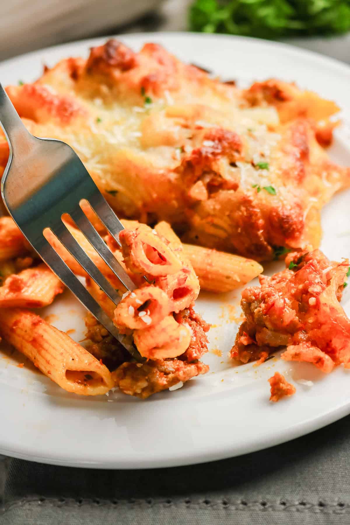 A fork lifting sausage pasta bake with meat sauce and melted cheese from a plate.