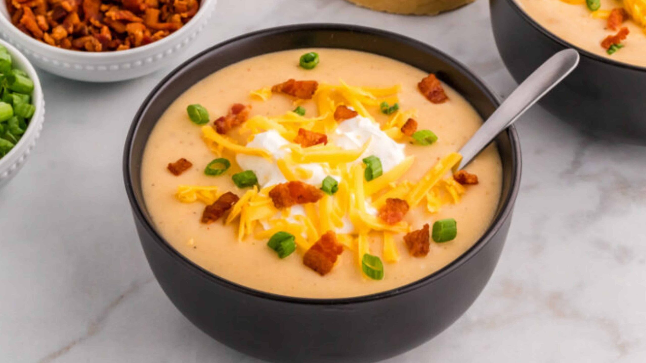 Bowl of potato soup topped with shredded cheese, bacon bits, sour cream, and green onions.